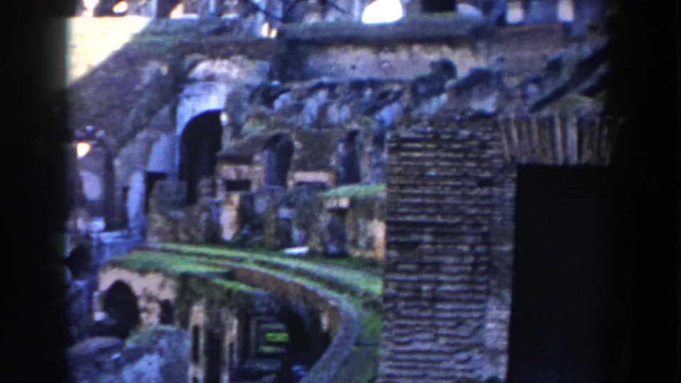1959 8mm view of the Colosseum interior in Rome, with brick masonry, arched ruin openings, and a green-topped curved structure.