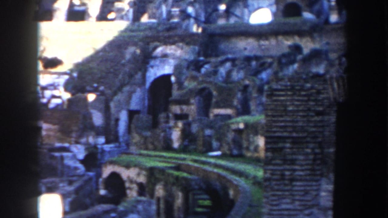 Sunlit Colosseum ruins with arches, grass, stone walls, and dark film-frame edges.