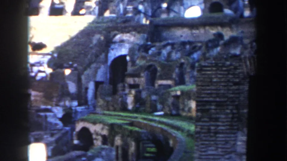 1959 8mm view inside the Colosseum in Rome, showing weathered arches, grassed ruin levels, and strong sun-shadow contrast.