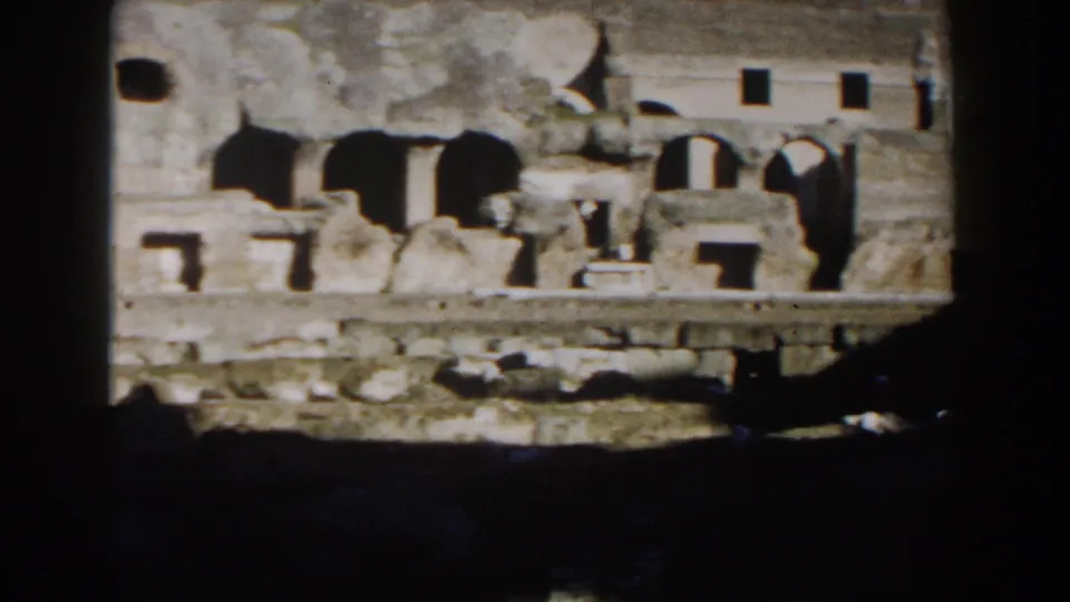 Late-1950s 8mm view of the Colosseum in Rome, centered on worn masonry, arched openings, and a low stone course.