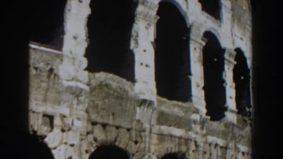 1959 Rome frame showing the Colosseum facade with large arched openings, pitted stone, and heavy shadow.