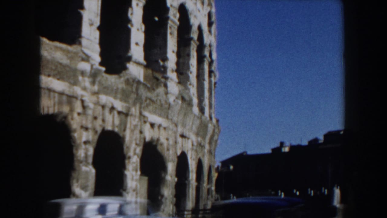 Colosseum exterior seen through dark 8mm frame borders with a blurred car passing below.