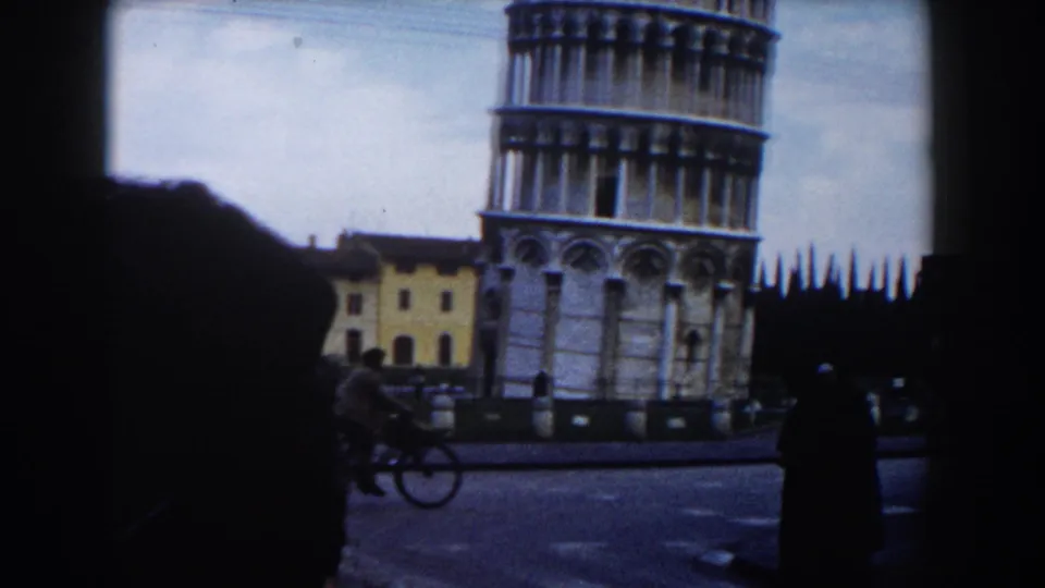 1959 Pisa travel frame showing the Leaning Tower, plaza activity, a cyclist, pedestrians, and surrounding buildings.