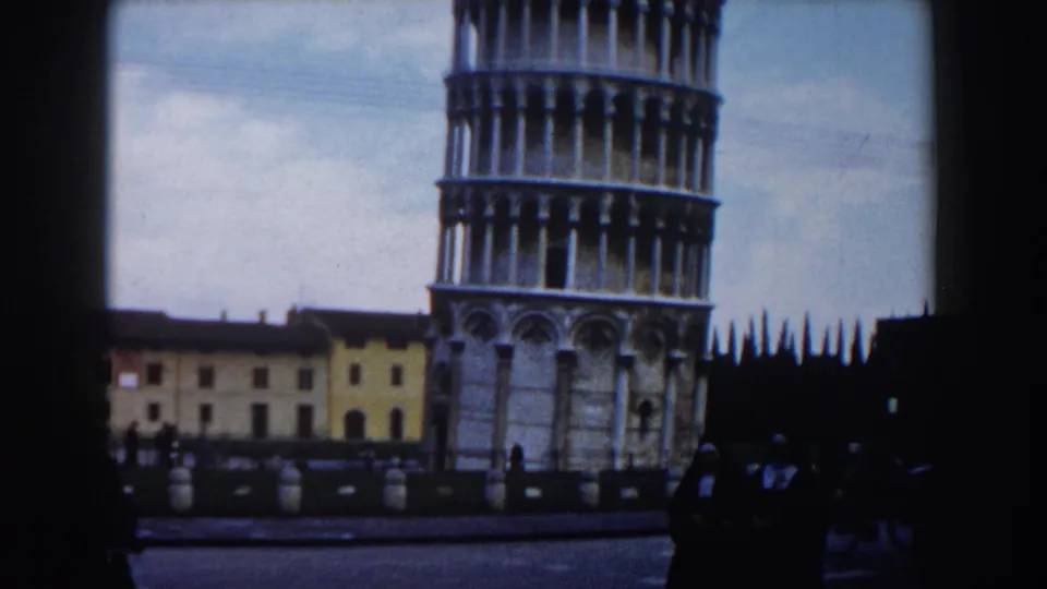 Pisa landmark view with the Leaning Tower, shadowed pedestrians, low buildings, and visible 8mm frame edges.