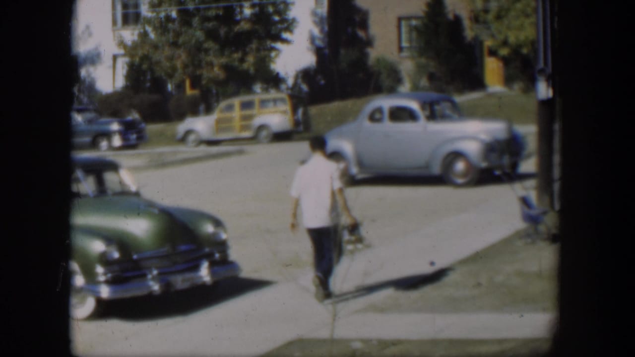 Man continues down the sidewalk past parked cars on a residential street.