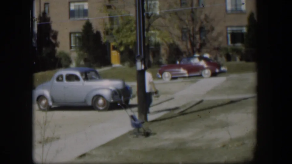 Near the end of the clip, the man moves toward the right edge of the Nevada sidewalk scene beside the stroller and vintage parked cars.