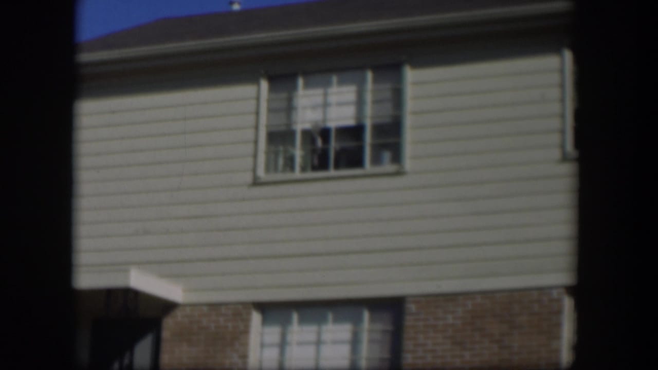 House upper story with pale siding, roof edge, divided window, and blue sky.