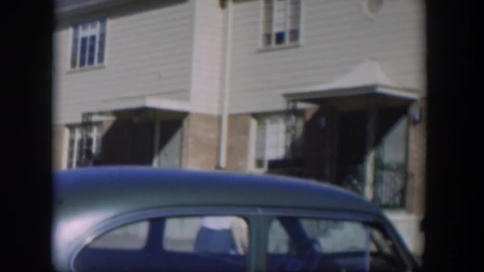 1954 Nevada residential frame showing a blue car beneath townhouse windows, siding, brickwork, and a covered entrance.