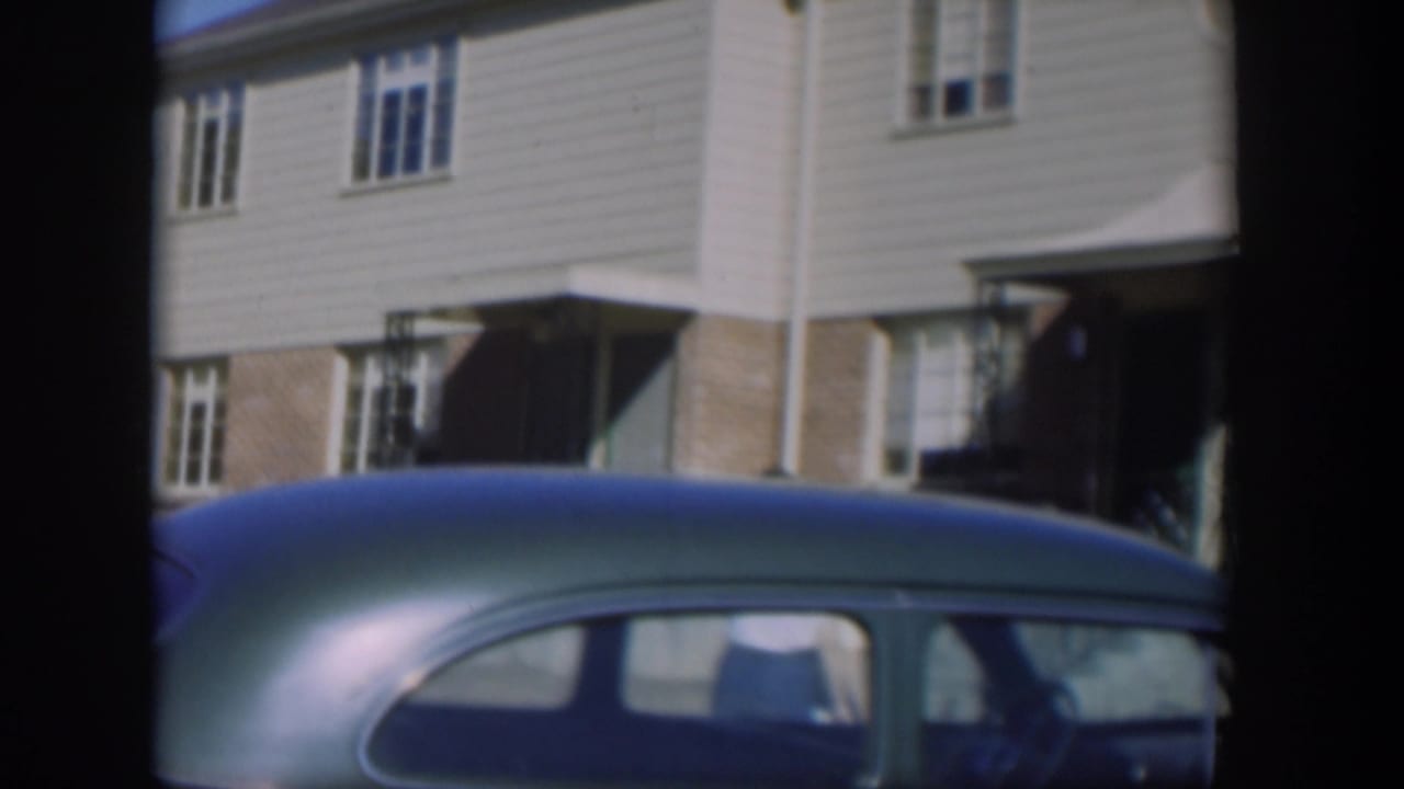 Two-story houses seen past the roof of a blue-green car.