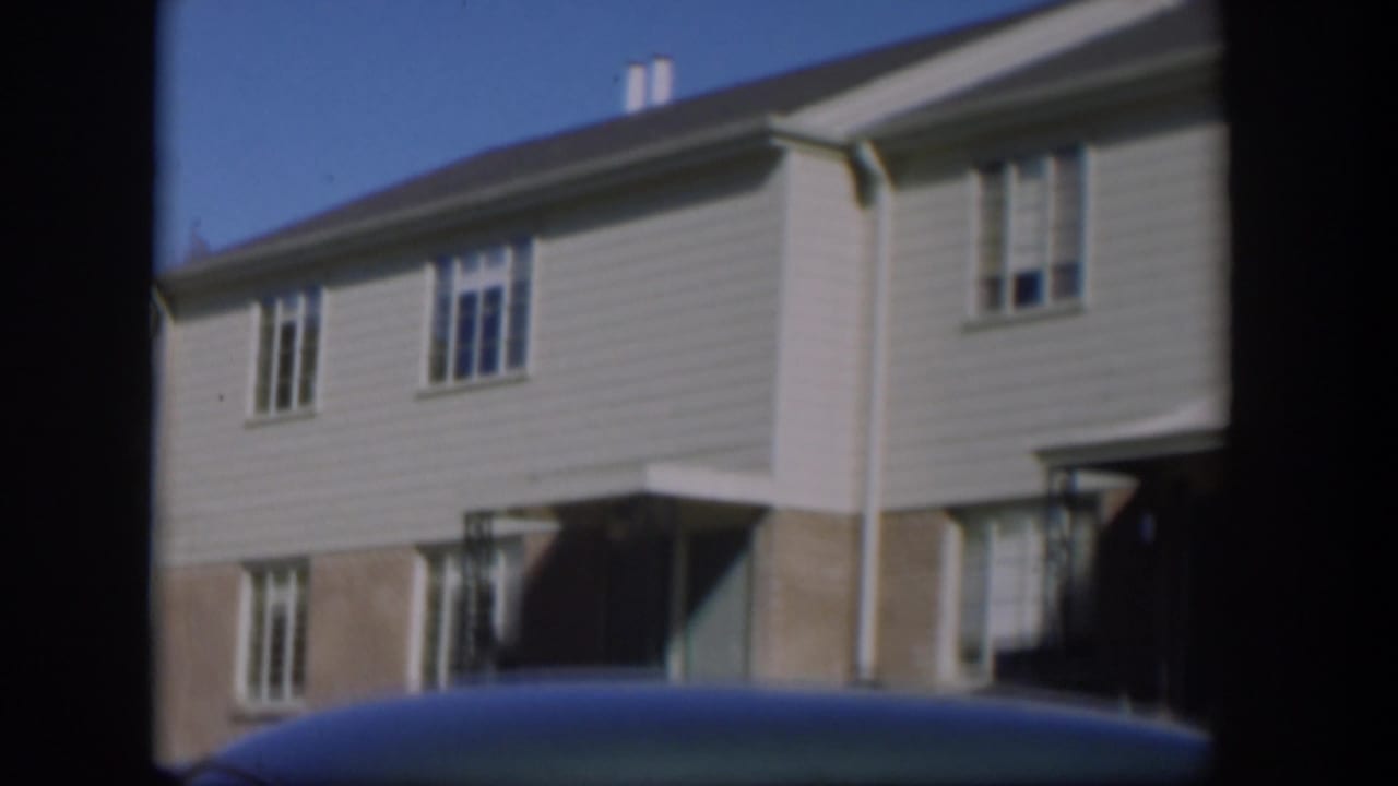 Two-story house with pale siding behind a car roof.