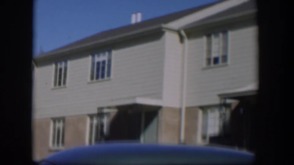 Nevada residential exterior from 1954, with pale siding, brick base, windows, and a car roof crossing the lower frame.