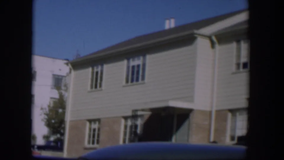 1954 Nevada home-movie view of a two-story residential building with windows and a dark foreground car roof.
