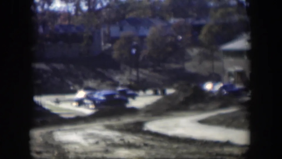 1954 Nevada home-movie frame showing cars near an apartment complex driveway, with trees, pavement, and soft 8mm exposure.