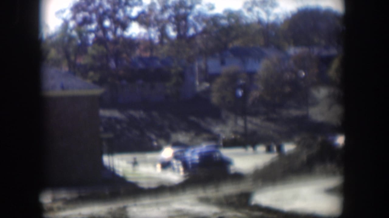 Blue sedan and another car near an apartment building and curved drive.