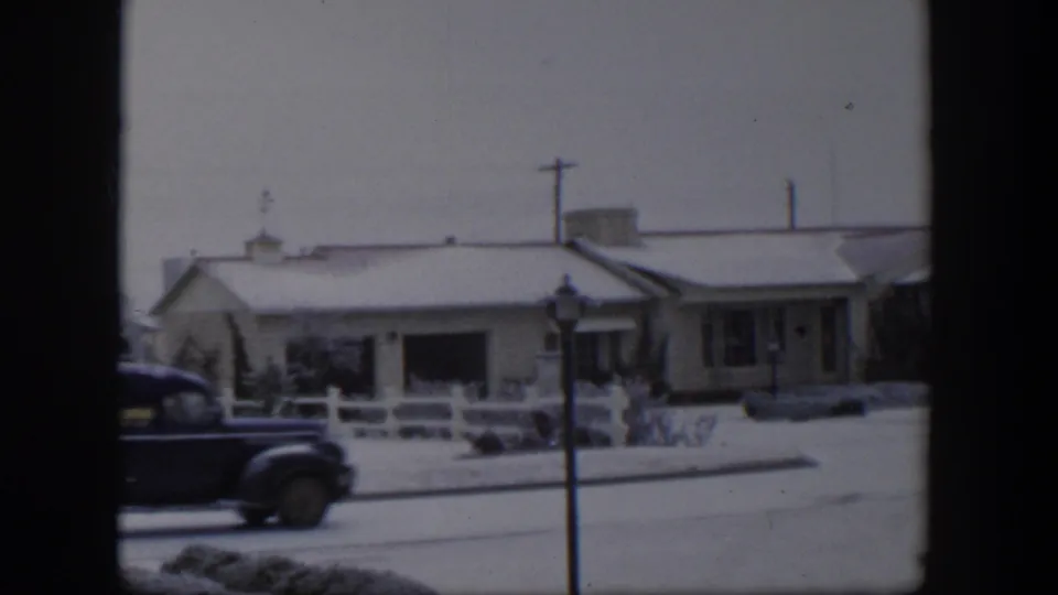 Blue delivery-style truck passes through a snowy Nevada neighborhood in this 1954 8mm home-movie frame.
