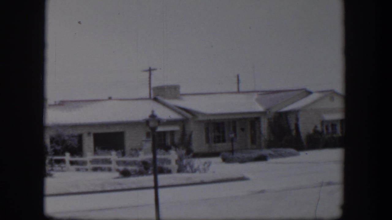 1954 Nevada 8mm frame showing snow-covered ranch-style homes, a white fence, a street lamp, and utility poles.