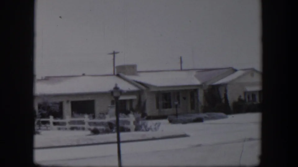 1954 Nevada 8mm frame showing snow-covered ranch-style homes, a white fence, a street lamp, and utility poles.