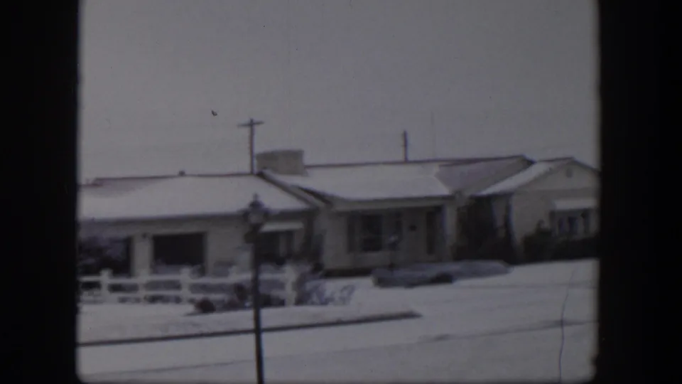 1954 Nevada home-movie frame of low suburban houses with snow on roofs and yards under an overcast sky.