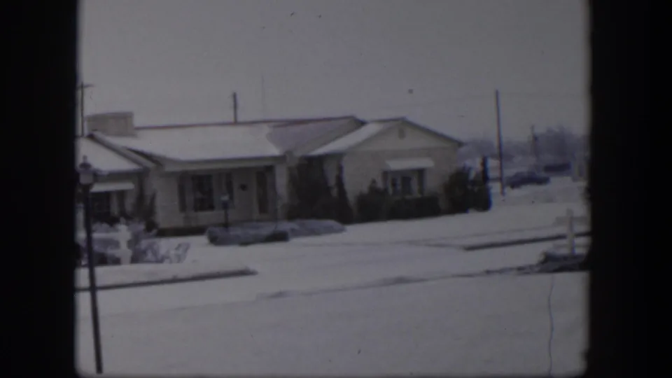 1954 Nevada residential view with snow on the roof and lawn, a street foreground, and a distant parked car.