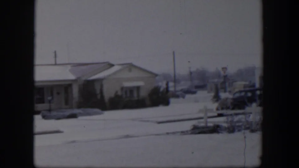 1954 Nevada frame with a cropped snowy house, winter street, parked cars, utility poles, and distant signs.