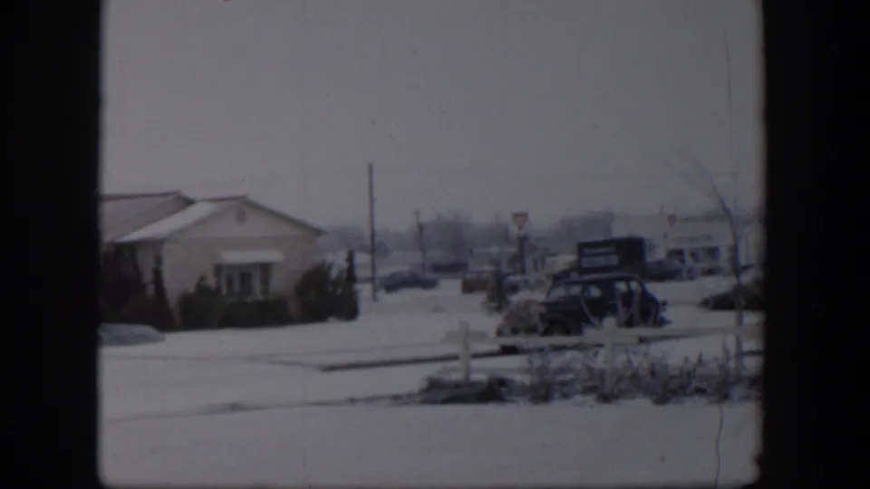 1954 Nevada home-movie view of a snowy residential street, low house, parked dark car, signs, and winter branches.