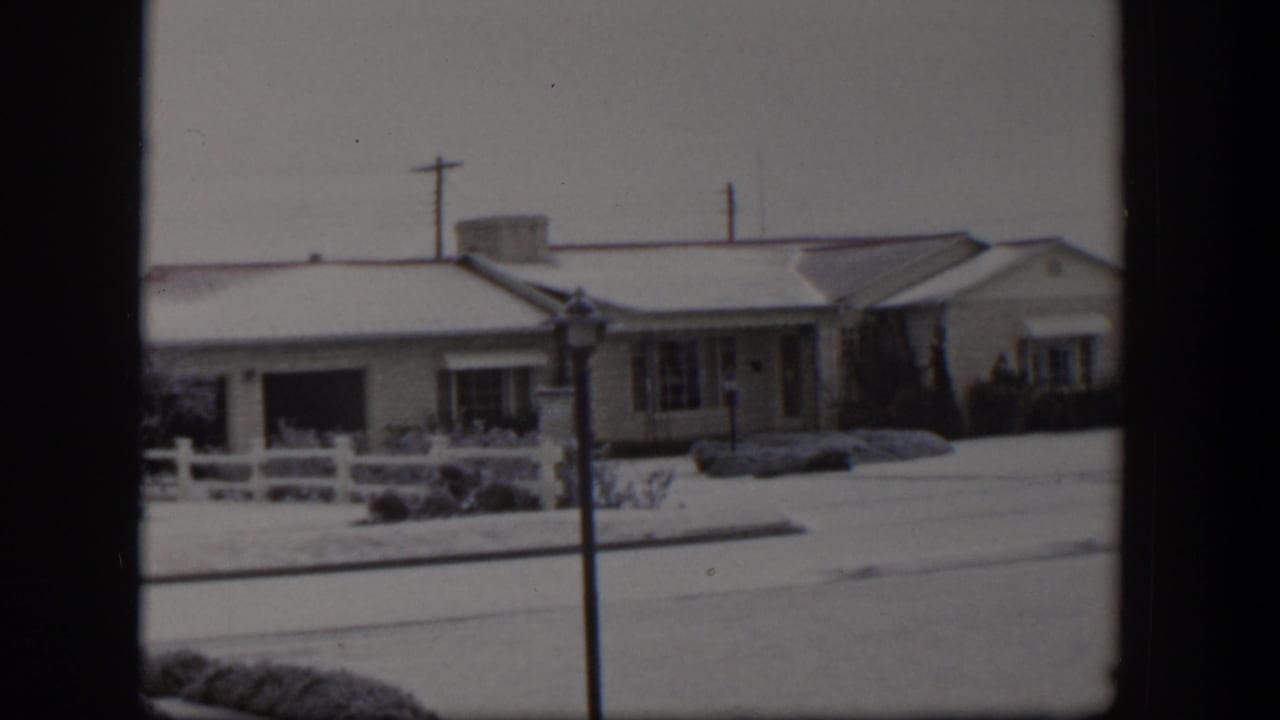 Snow-covered single-story houses behind a white fence and utility pole.