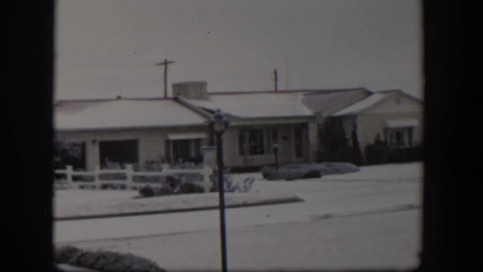 1954 Nevada home-movie frame showing snow on lawns and rooftops beside a quiet residential street.
