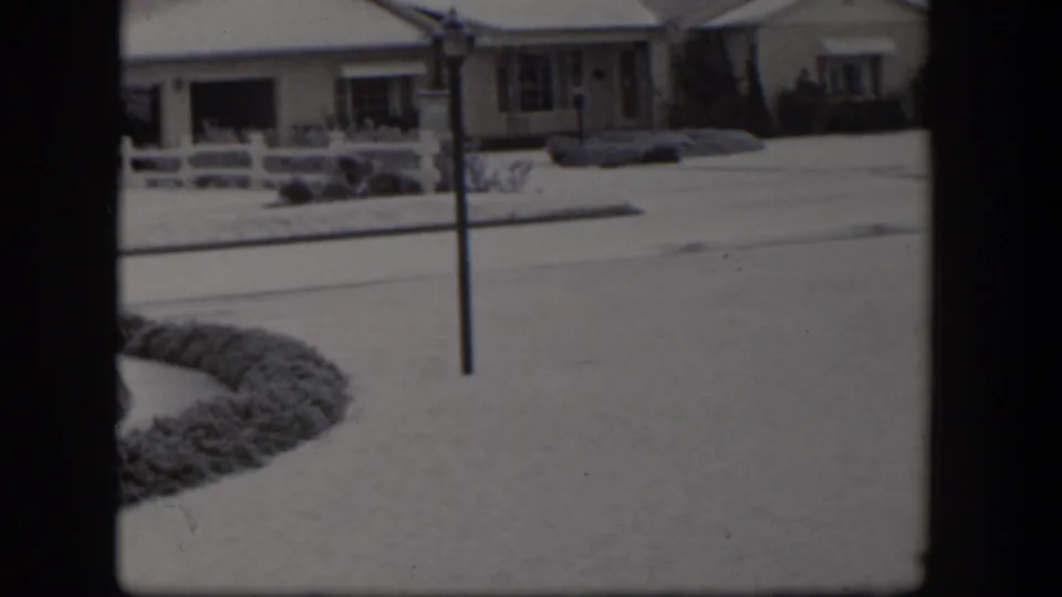 A snowy Nevada residential view shows a low house, white fencing, and an open front yard in 1954 footage.