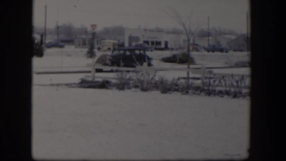A 1954 Nevada winter street view shows a parked dark sedan, fence, bare trees, and distant storefront-like buildings.