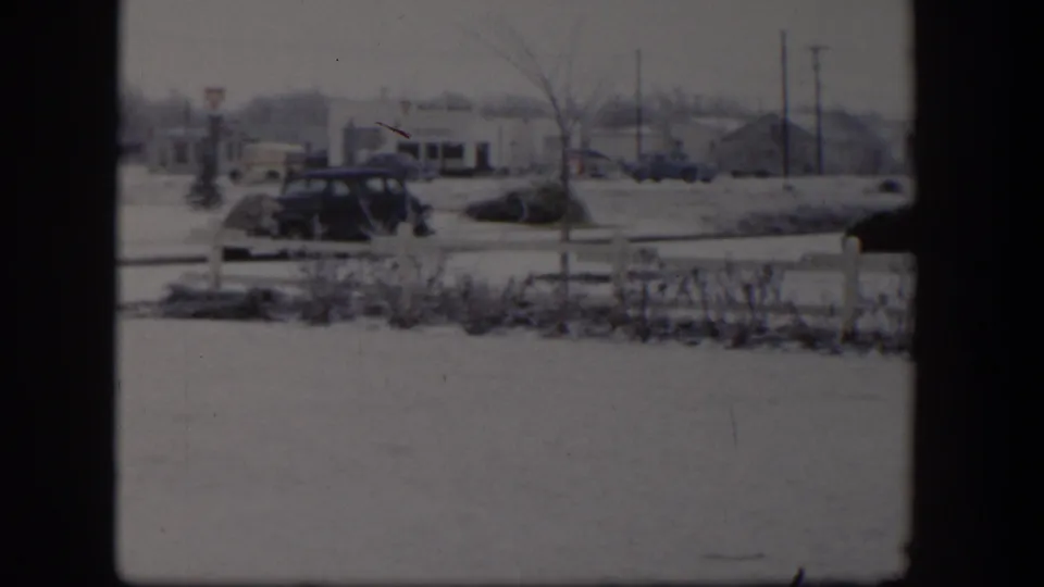 The final 1954 Nevada frame holds on a snowy roadside with a parked sedan and small buildings in the background.