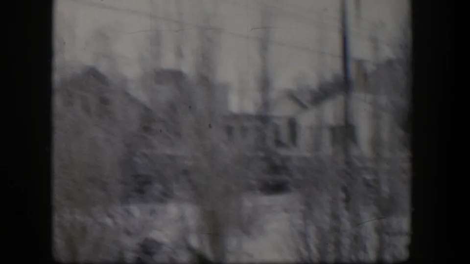 1954 Nevada 8mm frame with a blurred snowy residential view, bare trees, rooftops, shrubs, and dark window edges.