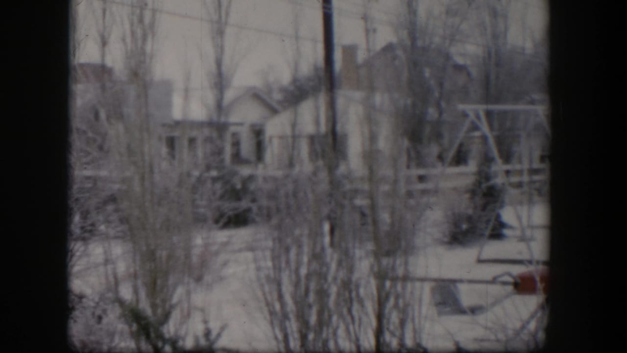 1954 Nevada 8mm frame showing a snow-covered suburban backyard with bare trees, a swing set, red seesaw, and houses beyond.