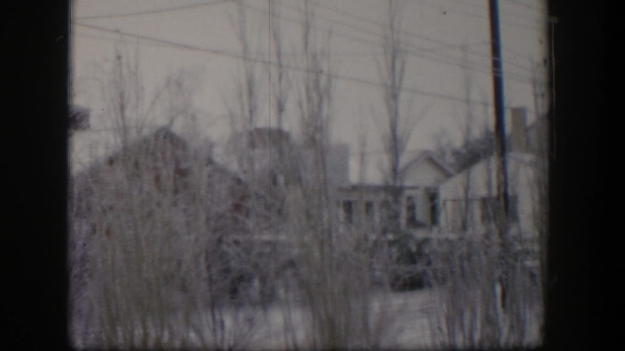Bare trees and utility lines cross a snowy view of small houses and sheds.