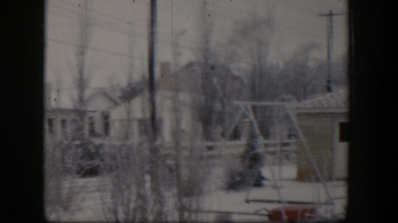 Snowy backyard with swing set, fences, utility poles, bare shrubs, and nearby houses.