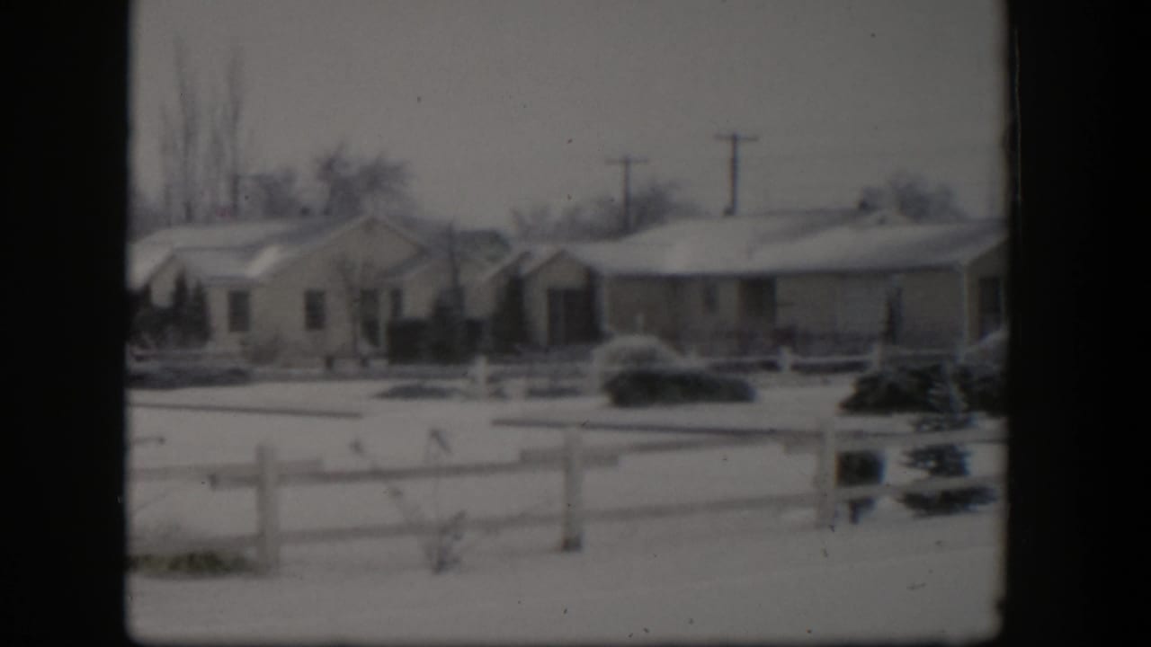 Snow-covered suburban houses behind a low wooden fence with utility poles in the background.