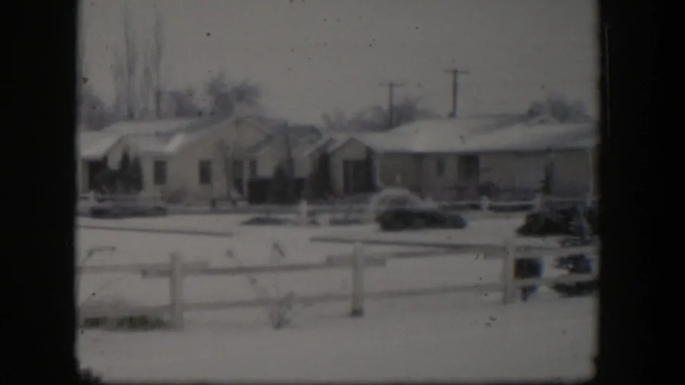 1954 Nevada suburban winter exterior with snow on roofs and lawns, low fencing, shrubs, and overhead utility poles.