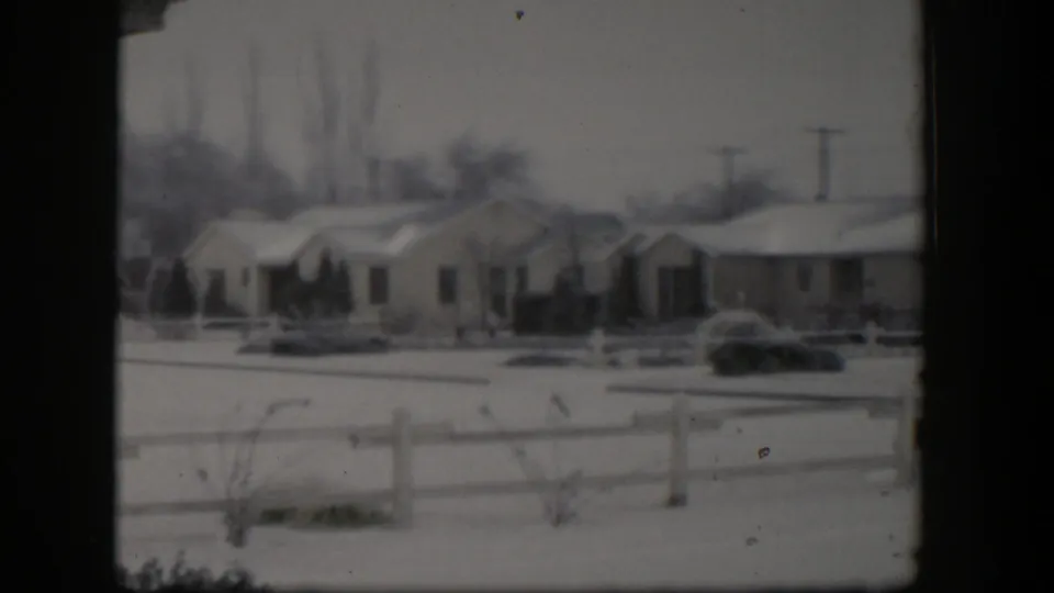 1954 Nevada home-movie view of a snowy suburban block, with houses set behind a fence and bare trees in the distance.