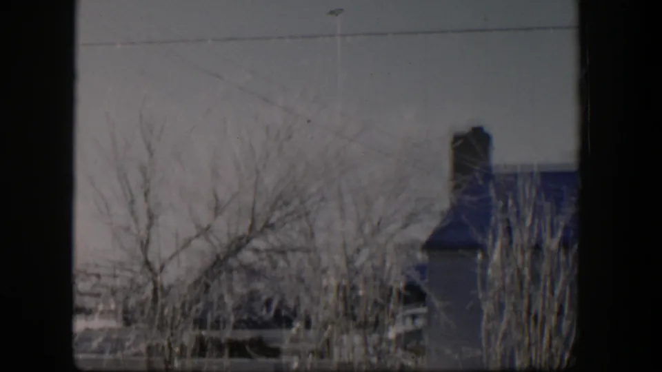 1954 Nevada 8mm frame showing leafless frosted trees, a fence, and a partial house exterior with a chimney in the background.