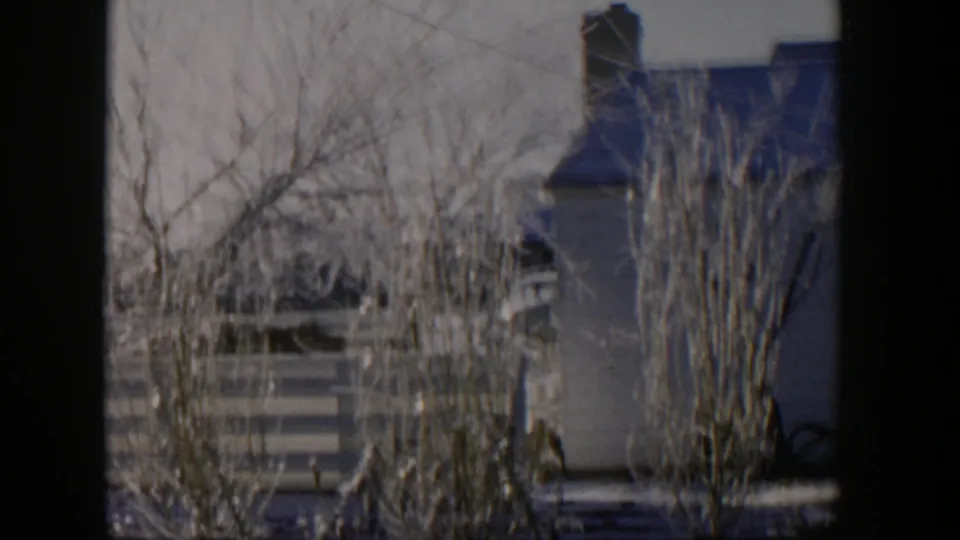 1954 Nevada 8mm frame with a house exterior, chimney, fence, and frost-covered trees sliding past the car window.
