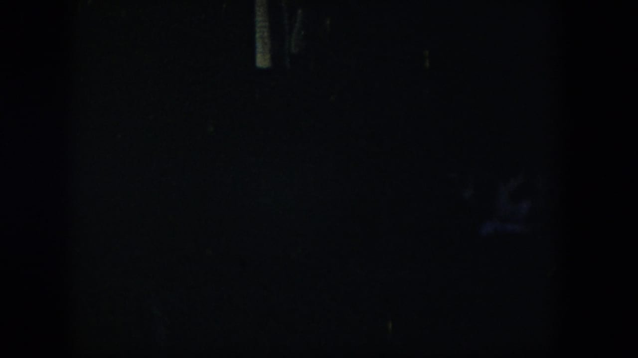 Dark room view with a small pale vertical mark and faint bluish object in shadow.