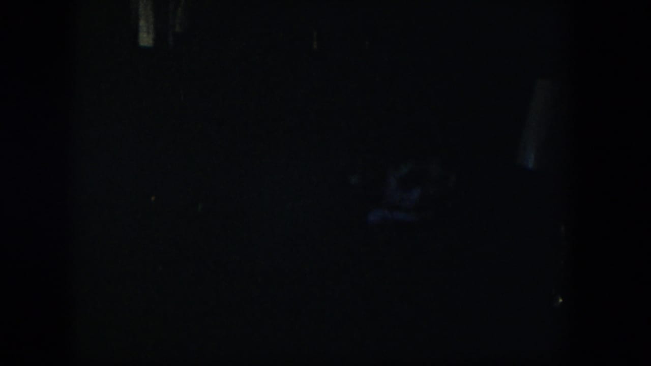 Nearly black interior frame with faint shapes and film grain.