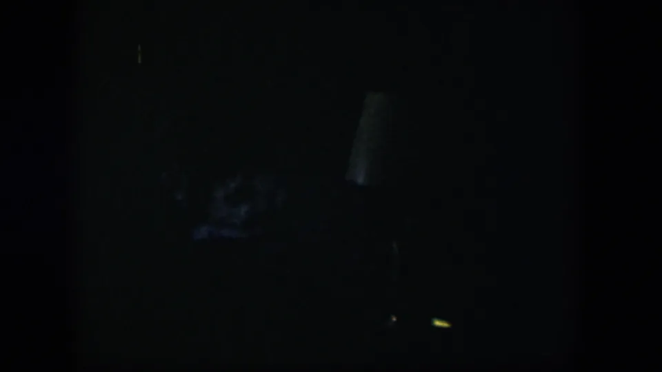 Very dark 1954 Nevada home-movie frame with indistinct interior shapes and low-light 8mm grain.