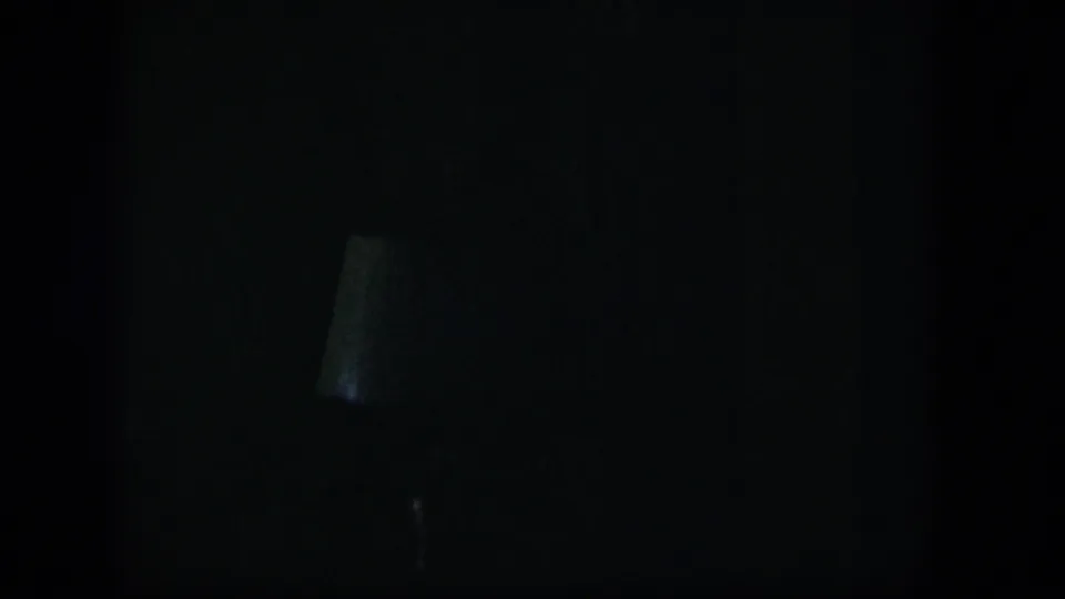Underexposed 1954 Nevada interior frame with a faint lampshade silhouette emerging from the darkness.