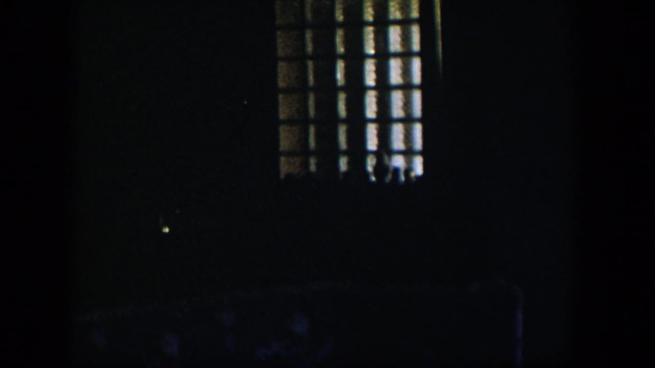 1954 Nevada 8mm frame showing a dim room with a barred or gridded window casting faint light into heavy shadow.