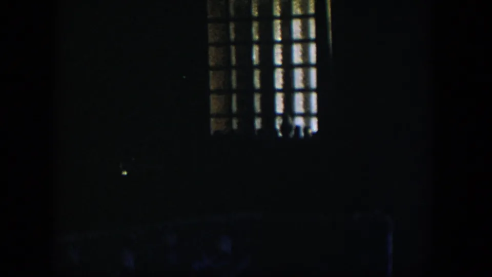 1954 Nevada 8mm frame showing a dim room with a barred or gridded window casting faint light into heavy shadow.