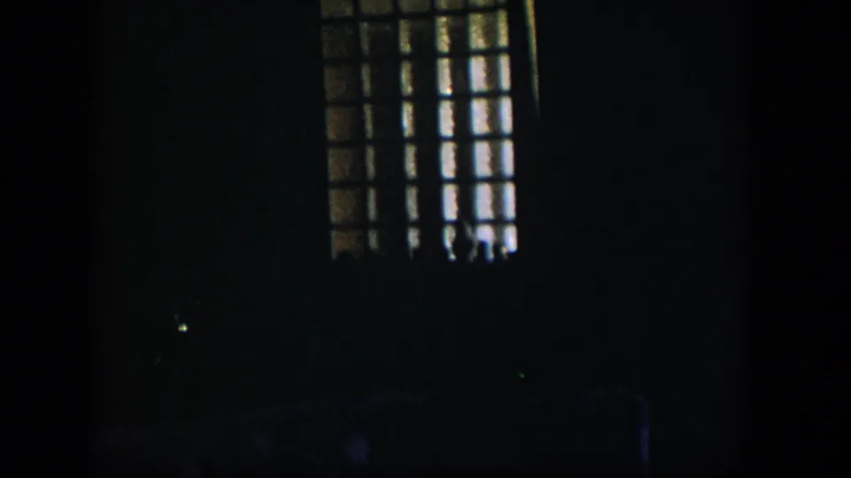 1954 Nevada 8mm frame with a gridded window partly visible at upper right and most of the room held in darkness.