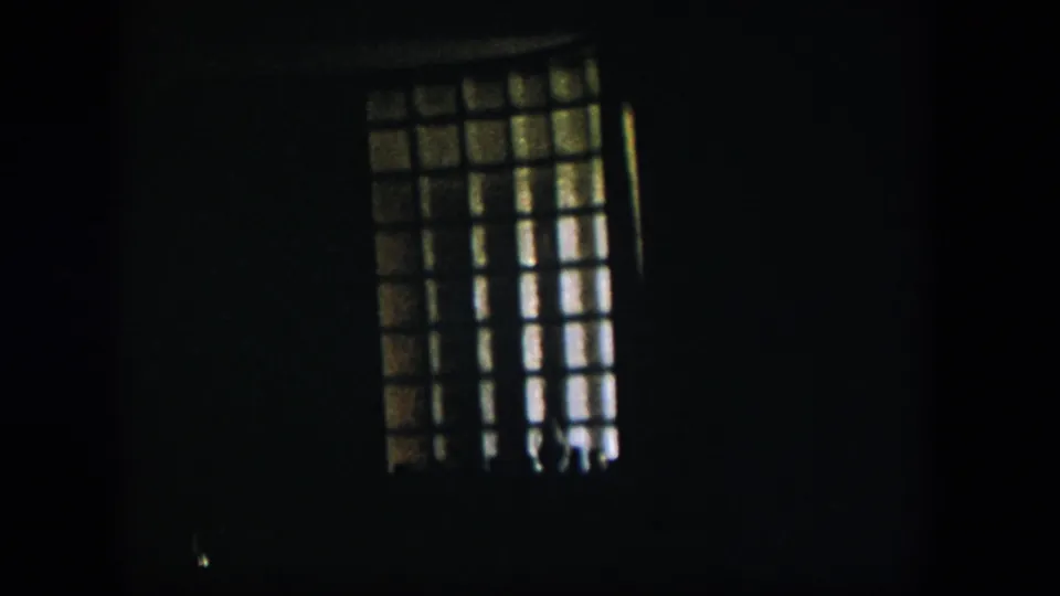 1954 Nevada 8mm frame showing a tall barred or gridded window at left, with the surrounding room nearly black.