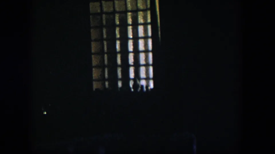 1954 Nevada 8mm frame showing a barred or gridded window glowing at upper right above a mostly obscured interior.