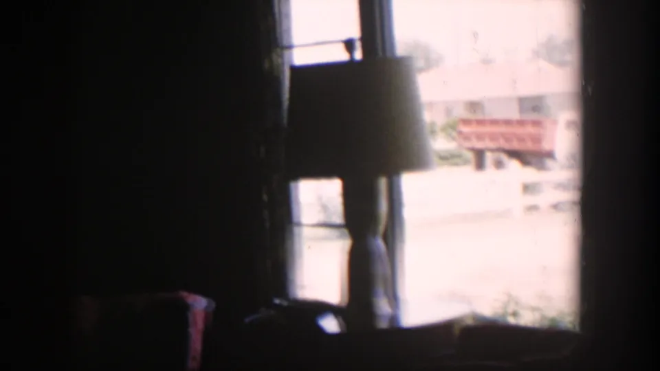 1954 Nevada interior with a lampshade silhouette against a bright window and a reddish bench outside.