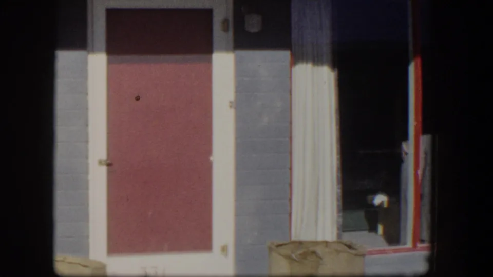 1954 Nevada frame centered on the red door and glass entry, with the dog partly visible near the doorway as the camera pans.